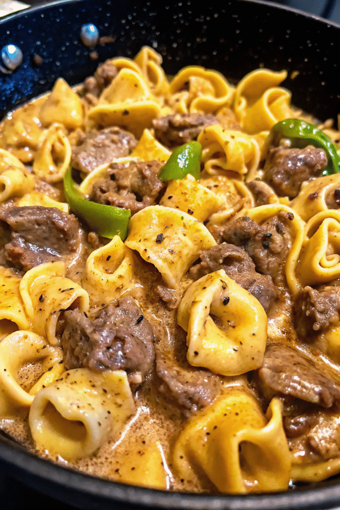 Plated cheesesteak tortellini with creamy provolone sauce garnished with fresh parsley and black pepper
