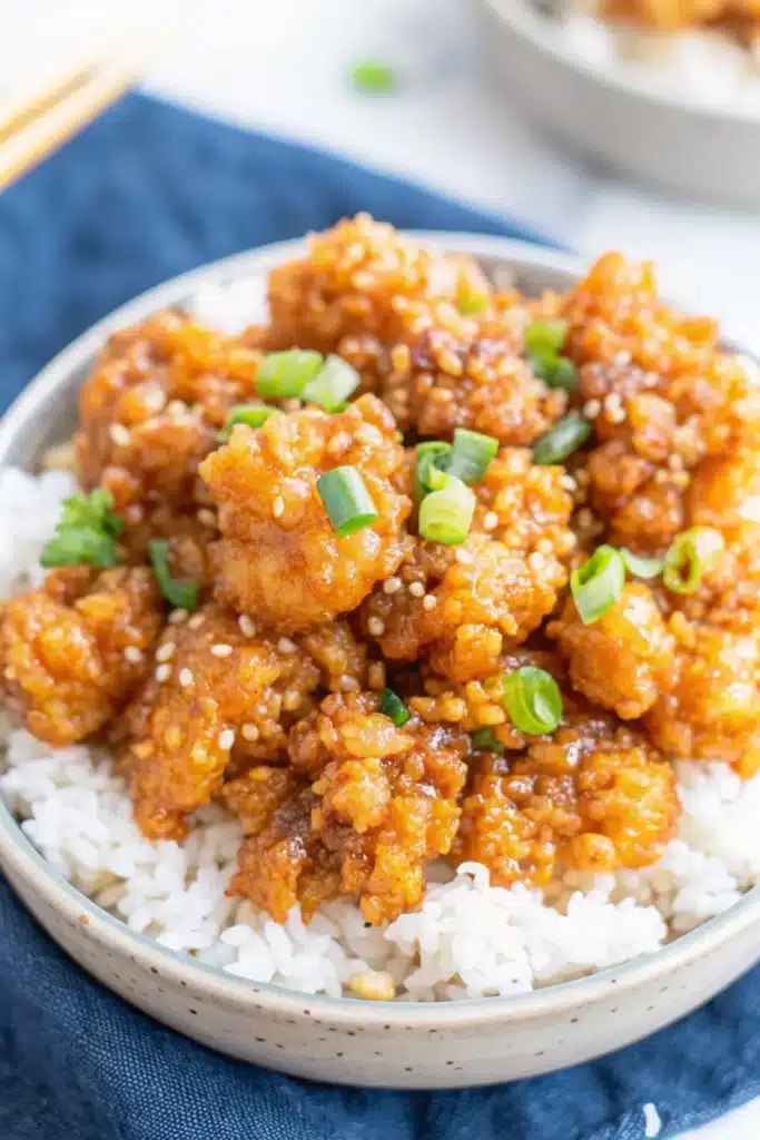 Plated crispy tofu with chopsticks on a wooden table alongside steamed broccoli and jasmine rice
