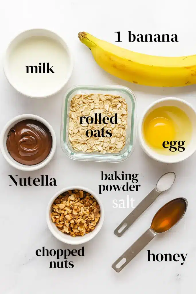 Rolled oats, milk, egg, banana, Nutella jar and baking powder on wooden kitchen table